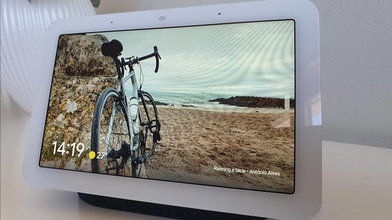 Google Nest Hub em cima de uma mesa, exibindo uma fotografia de uma bicicleta numa paisagem de praia